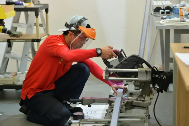 A focused construction worker operates a table saw while wearing protective gear inside a workspace in Flint.